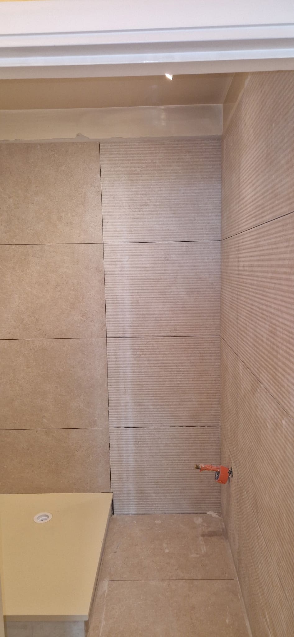 Mur de salle de bain en carrelage grand format, pose en cours sur colle peignée.