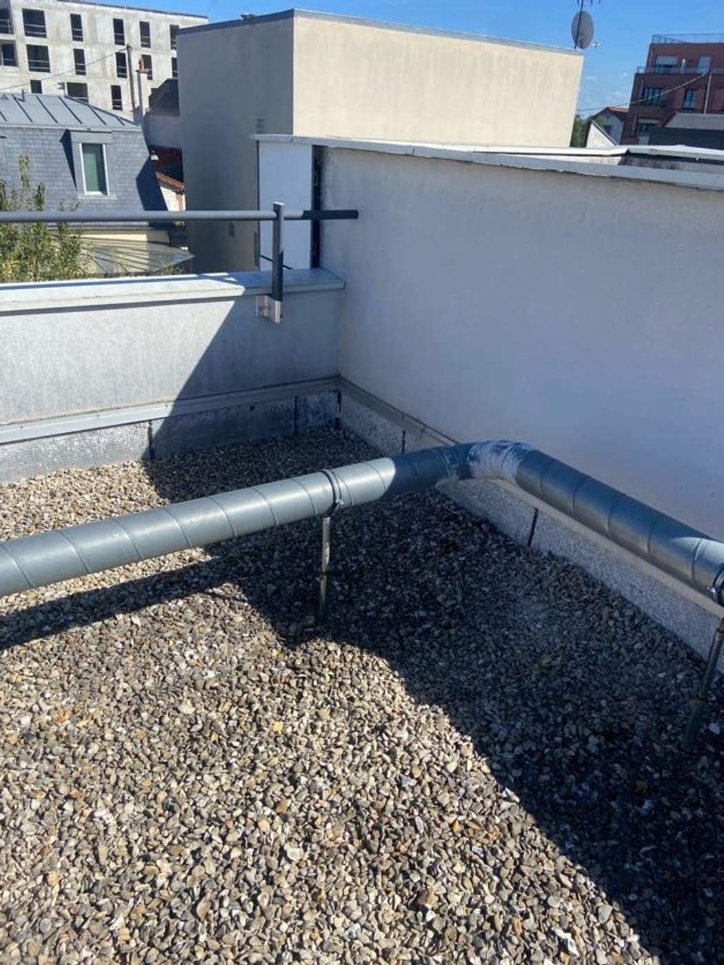 Conduit de ventilation en acier galvanisé posé sur une toiture-terrasse en gravillons.