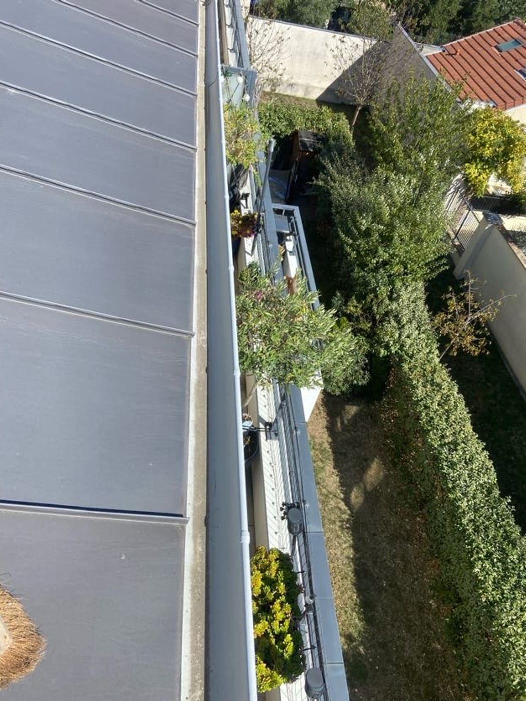 Chéneau longeant une toiture en zinc à joint debout au-dessus d’un jardin.