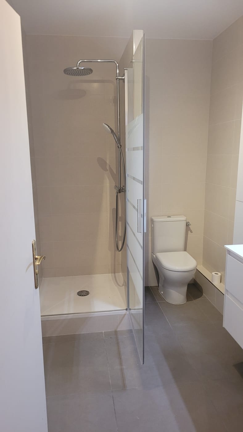 La même salle de bain après travaux : douche de plain-pied avec paroi vitrée, carrelage grand format et WC repositionné.