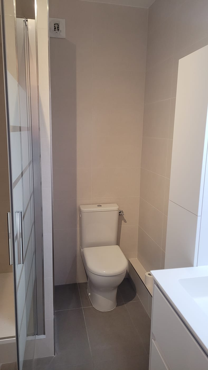 La même salle de bain après travaux : sol en grand format, WC neuf et paroi de douche posée.