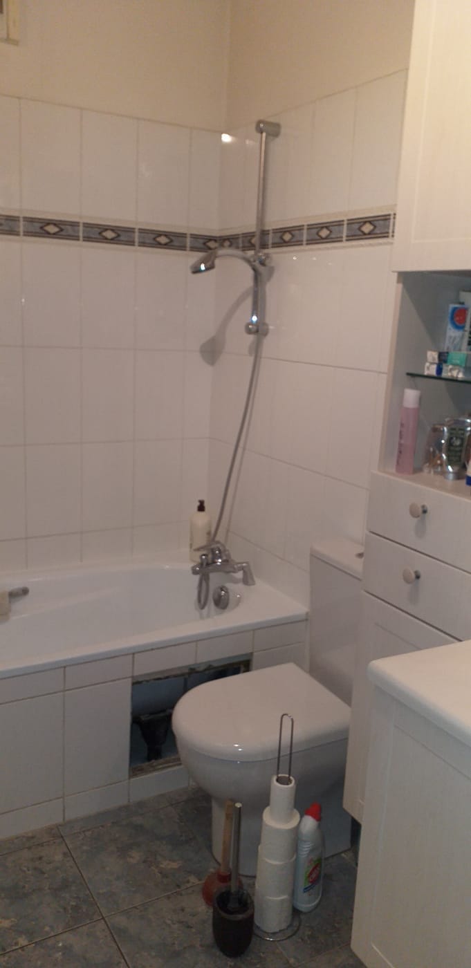 Salle de bain avant travaux : baignoire, colonne de douche murale et faïence blanche à frise.